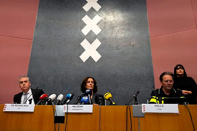 Woman and two men sitting behind a desk, speaking into microphones