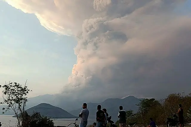 People watch a volcanic eruption with ash and smoke rising into the sky