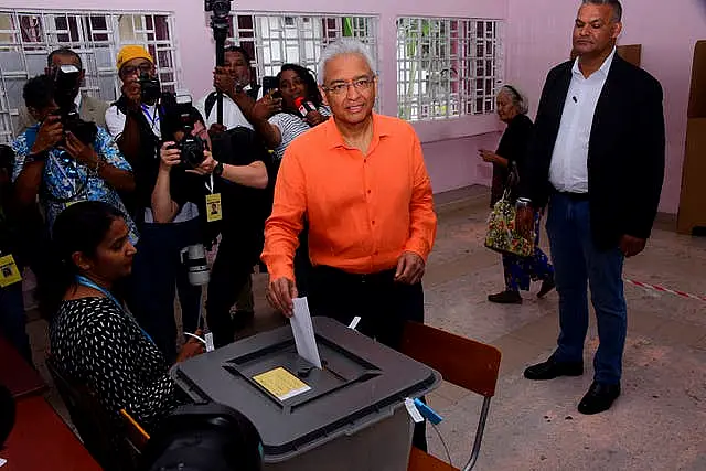 Pravind Jagnauth wearing orange shirt posts voting paper into ballot box