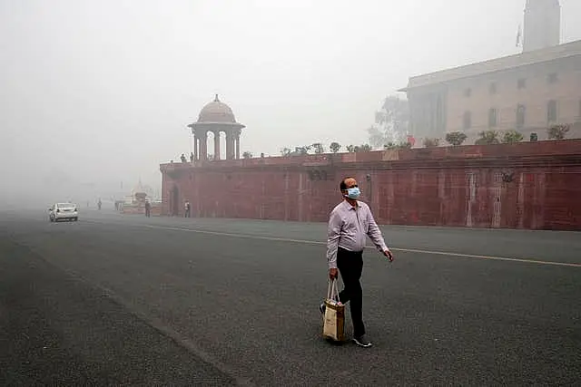 A office goer walks wearing a face mask amid a thick layer of smog in New Delhi