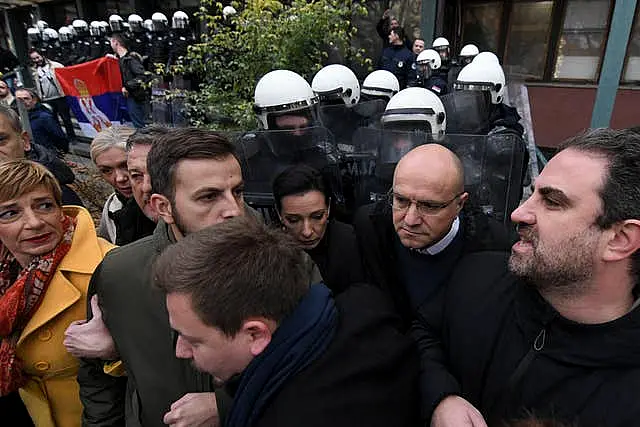 A line of protesters with white-helmeted riot police in the background