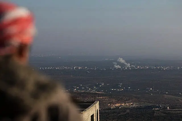 An observer watches as smoke rises amid fighting between opposition factions and Syrian government troops in Majdaliya