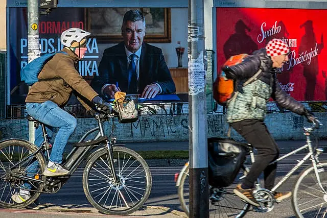 Cyclists ride past a poster of incumbent President Zoran Milanovic in Zagreb