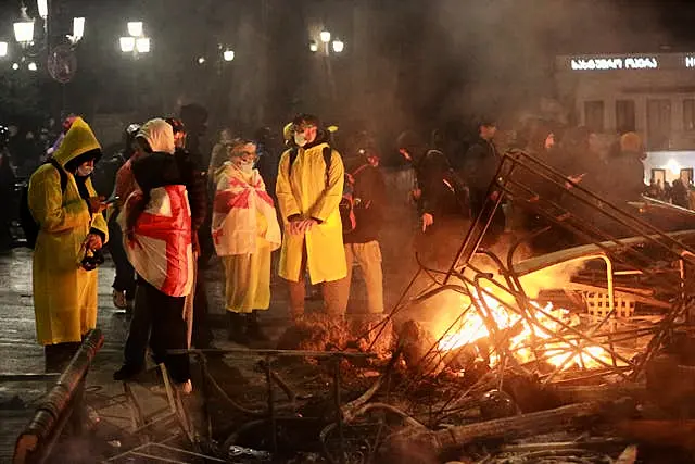 Demonstrators warm themselves next to a burning barricade 