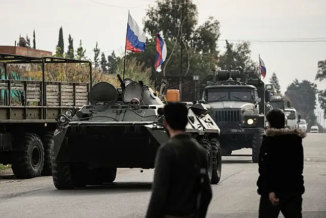 Syrian fighters watch Russian armoured vehicles driving past near the Hmeimim Air Base