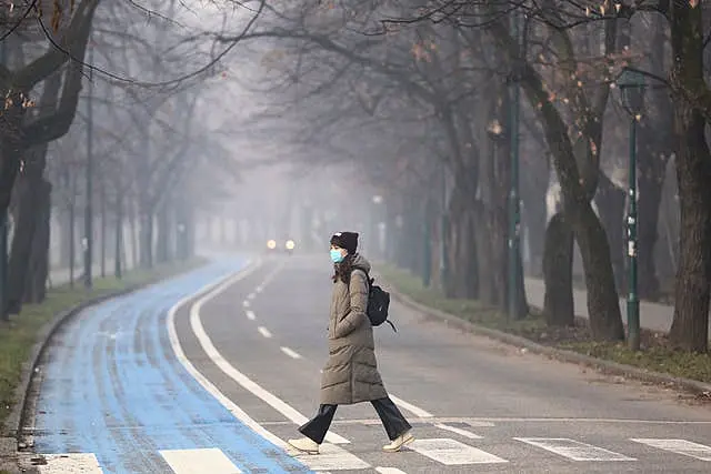 A woman wears a face mask shrouded by pollution haze as smog covers Sarajevo