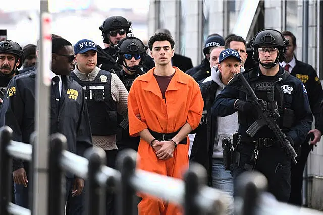 Luigi Mangione in cuffs and an orange prison suit is escorted to court by armed officers