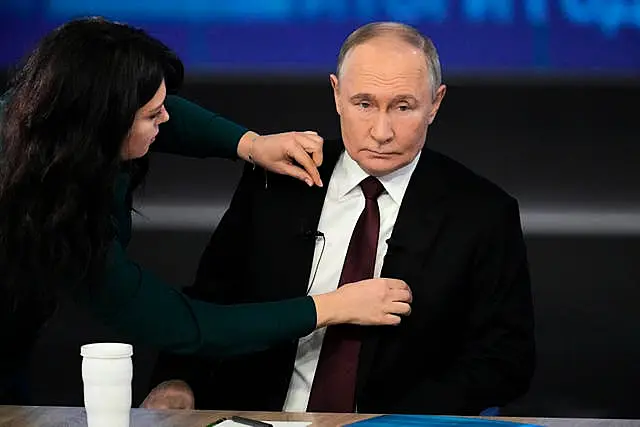 A woman adjusts Vladimir Putin's jacket as he prepares for his annual news conference