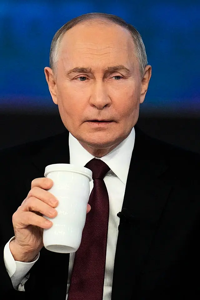 Vladimir Putin, holding a drink, listens to a question during his annual news conference