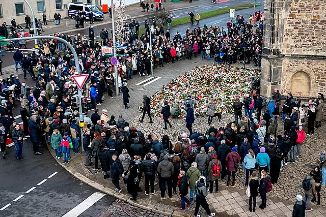 Crowd of people gathered around makeshift memorial of flowers and candles