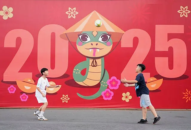 Two boys play football in front of a billboard welcoming the New Year 2025 in Ho Chi Minh city, Vietnam