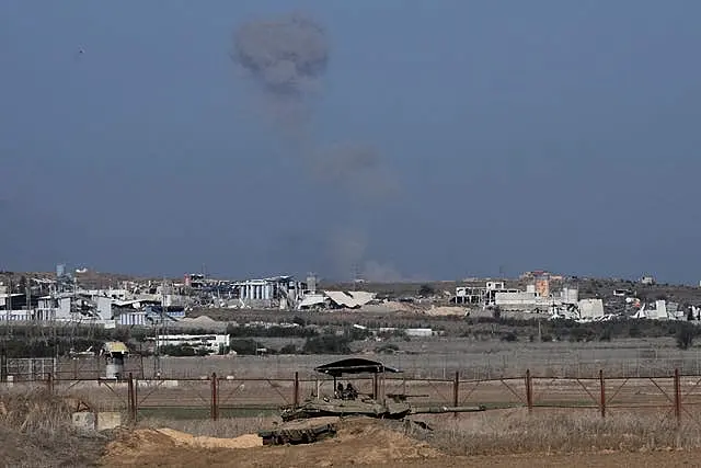 An Israeli tank sits on the Israeli-Gaza border, with a cloud of smoke inside the Gaza Strip in the background