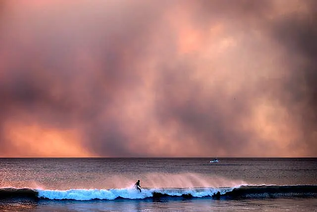 A surfer takes off on a wave in Santa Monica during sunset under a blackened sky from the Palisades fire