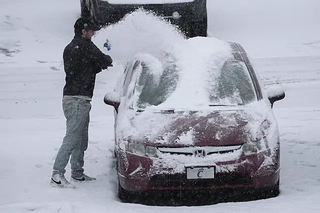 A person dusts snow off a car 