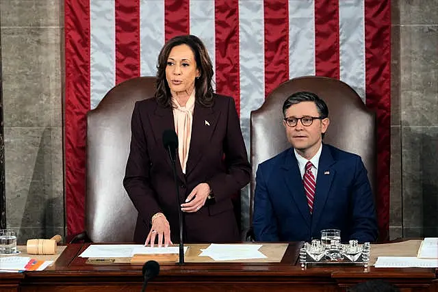 Kamala Harris and Mike Johnson sit in front of a huge American flag