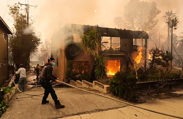 Pedestrians help a firefighter stretch a hose as an apartment building burns in Pasadena 