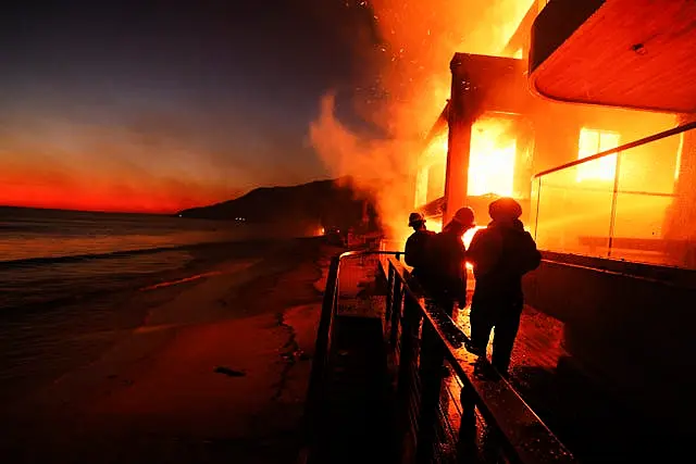 Firefighters work from a deck as the Palisades Fire burns a beachfront property in Malibu