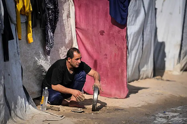 A man washes a tray outside a tent at a camp for displaced Palestinians in Deir al-Balah, central Gaza Strip 