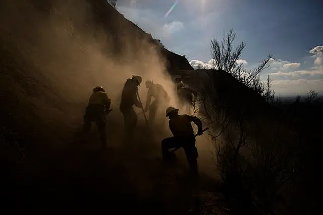 Bombeiros trabalham em meio à poeira enquanto limpam detritos de incêndio