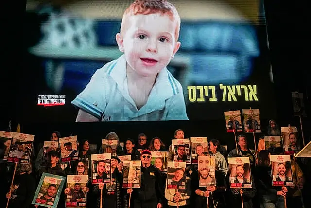 Demonstrators hold portraits of hostages held by Hamas in the Gaza Strip as a video featuring Ariel Bibas is played behind them