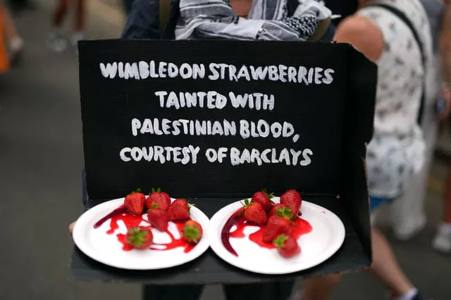 Two plates of strawberries covered in red sauce. There's a black sign above that says 'Wimbledon strawberries tainted with Palestinian blood, courtesy of Barclays