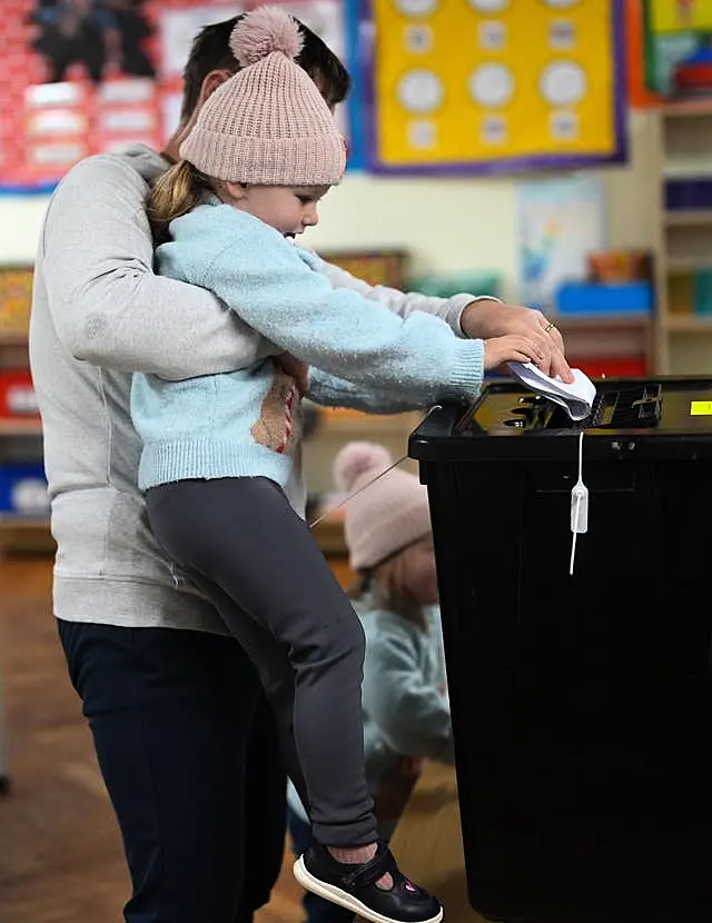 A woman lifts up a young girl so she can put a vote in a ballot box