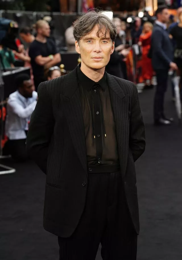 A man wearing a dark suit stands in front of a crowd