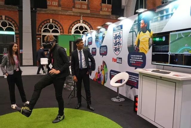 Prime Minister Rishi Sunak watches a man using a VR headset at an FA stand at the Exhibitor’s Hall at the Manchester Central convention complex, during the Conservative Party annual conference
