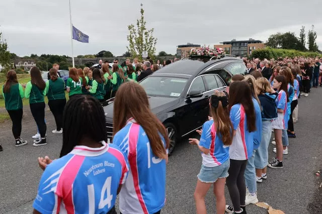 Young girls from Newtown Blues Ladies GFC and Tremonfeckin Celtic FC, and mourner during a minute's applause