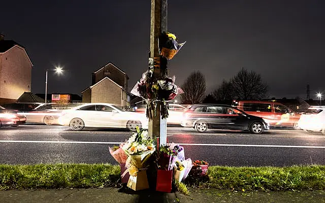 Floral tributes attached to a lamppost with cars in background