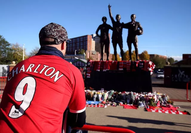 A fan kneels in front of the Manchester United Trinity statue at Old Trafford