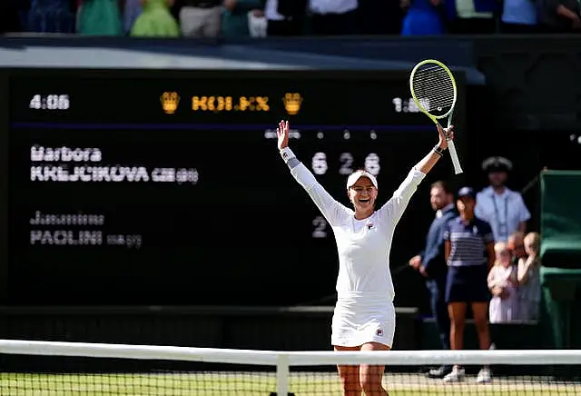 Barbora Krejcikova raises her arms and racket in the air in celebration in front of the net