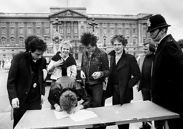 Black and white image of Sex Pistols and manager Malcolm McLaren signing a recording contract outside Buckingham Palace