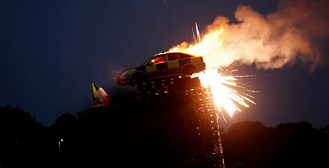 A mock police car is set alight on top of a bonfire