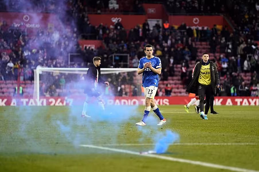A blue flare lands on the pitch as Seamus Coleman applauds the Everton fans