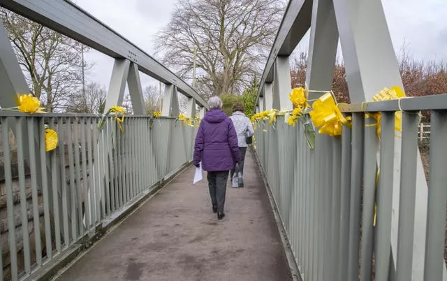 People walk past yellow ribbons tied to a bridge over the River Wyre