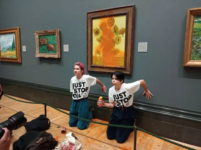 Two women kneeling in front of a defaced painting