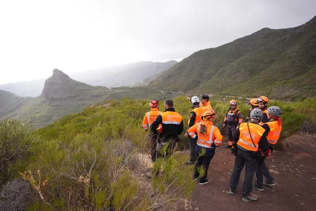 Members of a search team dressed in hi-vis jackets stand in a group with a mountainous area behind them