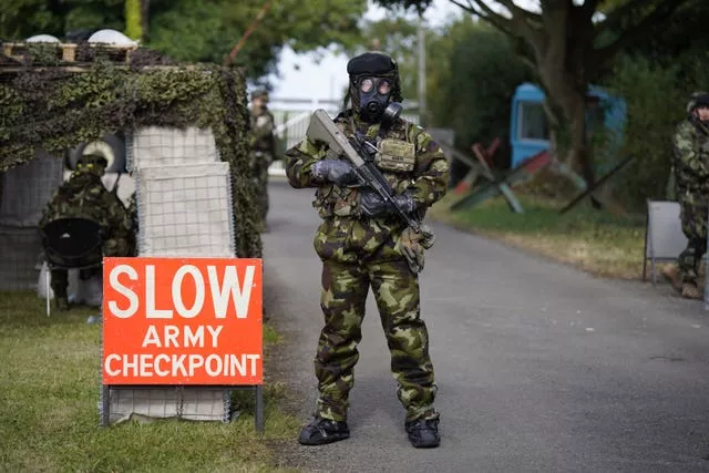 A soldier wearing a chemical, biological, radiological and nuclear (CBRN) suit and holding a weapon next to a red and white Army checkpoint sign