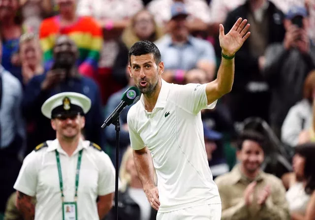 Novak Djokovic sarcastically waves at fans as he speaks into a microphone on Centre Court