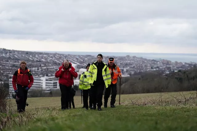 Uniformed police officers with search team members on a grassy slope near Brighton. 