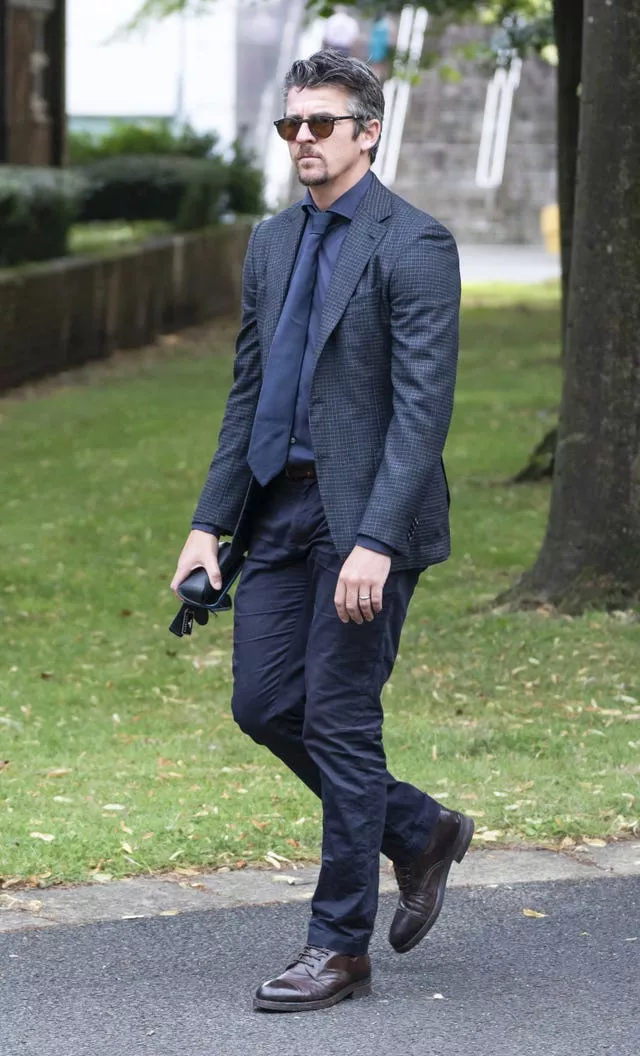 Joey Barton in dark suit, tie and sunglasses walking along a pavement