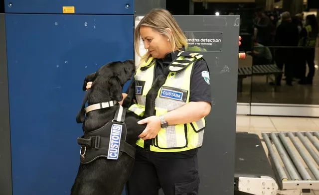 Customs officer smiles while a black sniffer dog jumps to rest its front paws on her chest