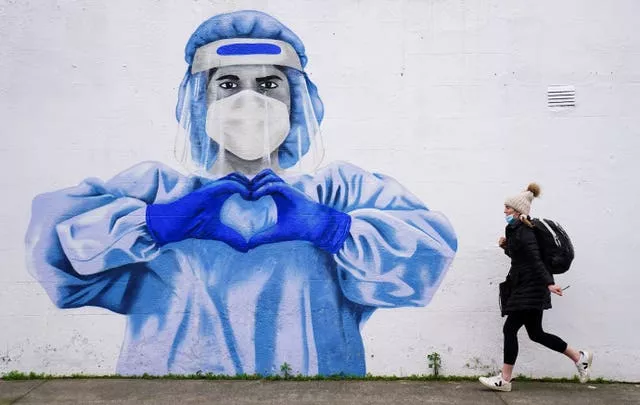 A woman walks in front of a mural of a frontline worker in Dublin