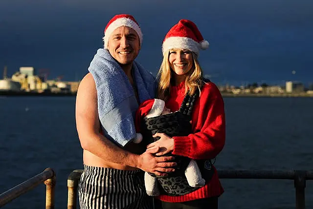 A couple and a baby all wearing Father Christmas hats