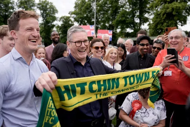 Sir Keir Starmer, surrounded by supporters, holds up a Hitchin Town FC scarf 