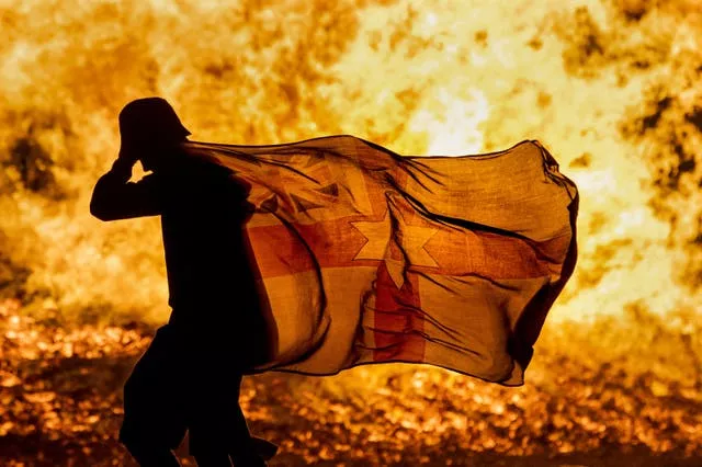 A young man carries a Northern Ireland flag in silhouette past the burning Craigyhill loyalist bonfire in Larne, Co Antrim, on the Eleventh Night