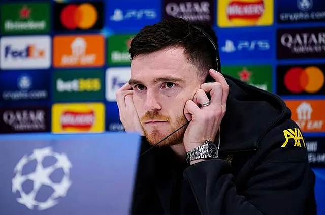 Andy Robertson holds headphones on his ears as he speaks to the media