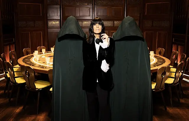 Claudia Winkleman standing between two hooded figures