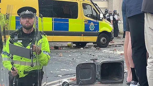 A police officer holding a riot shield in front of a police van